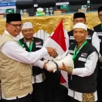 Kabid Penerimaan dan Pemberangkatan PPIH Embarkasi Aceh, Ahmad Yani menyerahkan perlengkapan kloter 7 pada almarhum Manshur (peci putih), Selasa, 4 Juni 2024. Foto: Istimewa