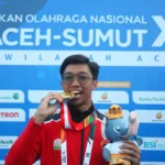 Atlet selam kolam Aceh Muhammad Iqbal menggigit medali emas yang diraihnya di nomor 400 meter bifin putra PON XXI-Aceh Sumut 2024. Foto: Istimewa